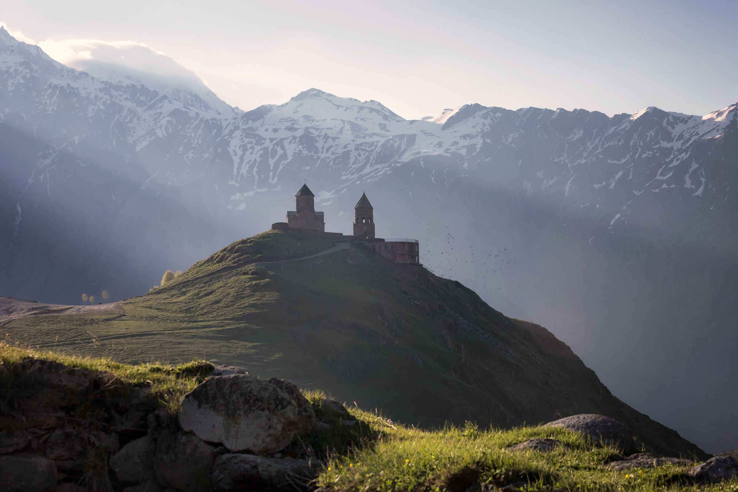 Gergeti Trinity Church standing alone beneath Mount Kazbek as sunrays break through cloud